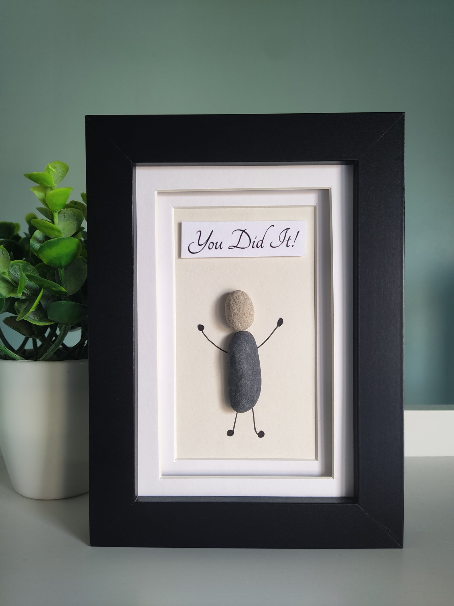A framed artwork with the text 'You Did It' accompanied by a silhouette of a person made from pebbles