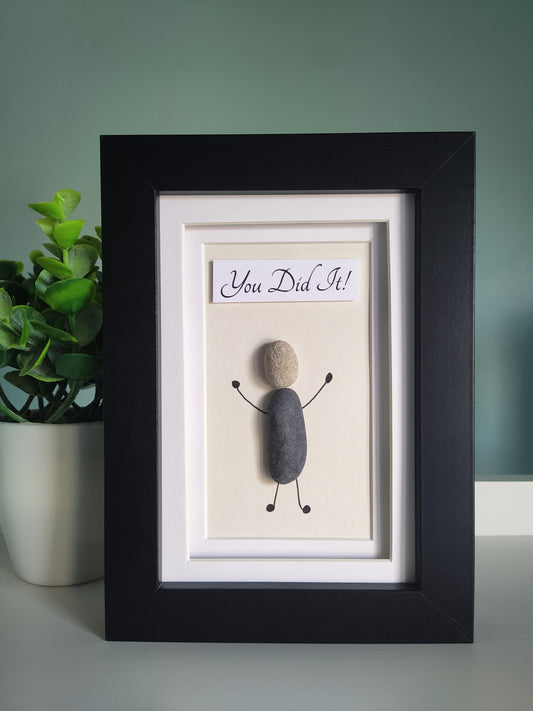 A framed artwork with the text 'You Did It' accompanied by a silhouette of a person made from pebbles