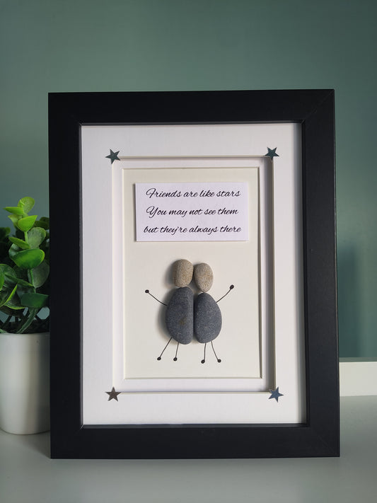 A framed artwork with two figures made from pebbles in a black frame, with the text 'Friends are like stars, You may not see them but they're always there' and surrounded by decorative stars.